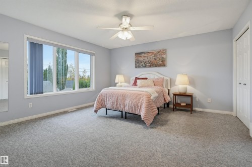 Expansive carpeted room featuring a large window, ceiling fan with integrated lighting, and a built-in closet with bi-fold doors - 7521 111 Avenue Nw, Edmonton, AB 