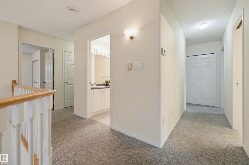 Carpeted hallway with a wood-finish handrail, white balusters, and a wall-mounted sconce - 7521 111 Avenue Nw, Edmonton, AB 