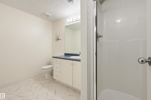 White tiled flooring, vanity with integrated sink, chrome faucet, wall-mounted mirror, and a standing shower with a clear enclosure - 7521 111 Avenue Nw, Edmonton, AB 