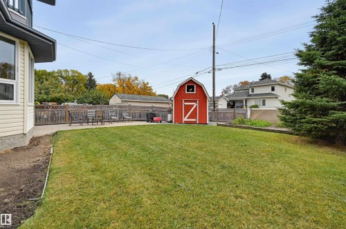 Spacious lawn with a red barn-style shed, concrete patio, and fenced perimeter - 7521 111 Avenue Nw, Edmonton, AB 
