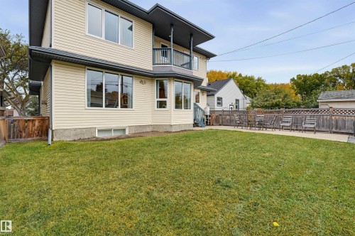 Rear exterior featuring light-toned horizontal siding, multiple windows, a balcony, a ground-level patio area, and a large grass lawn - 7521 111 Avenue Nw, Edmonton, AB 
