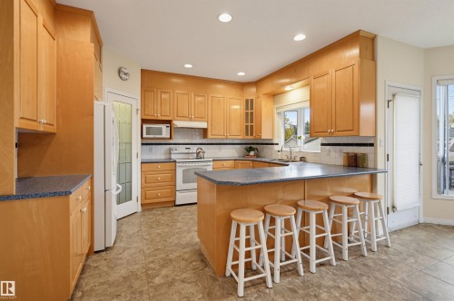 Kitchen featuring extensive light wood cabinetry, recessed lighting, a built-in microwave, white tile backsplash, and a counter-height island with seating - 7521 111 Avenue Nw, Edmonton, AB 