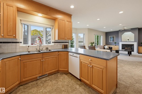 Open-concept kitchen featuring light wood cabinetry, stone-finish countertops, stainless steel sink, and tile flooring - 7521 111 Avenue Nw, Edmonton, AB 