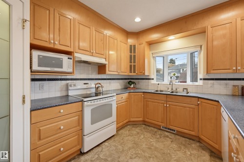 Kitchen featuring wood-finish cabinetry, solid surface countertops, a tile backsplash, and a double basin sink - 7521 111 Avenue Nw, Edmonton, AB 