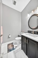 White tile flooring, dark vanity with white countertop, sleek circular mirror, and modern wall-mounted light fixture - 
