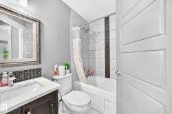 Vanity with integrated sink, mosaic tile backsplash, framed mirror, and a shower-over-tub with tile surround and dark accent strip - 