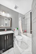Bathroom featuring a dark vanity with a white countertop, a white toilet, and a white tiled shower-tub combination with a dark mosaic accent - 