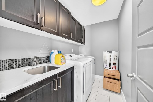 Laundry area featuring upper and lower cabinetry, a built-in sink, and tile flooring - 12730 118 Street Nw, Edmonton, AB 