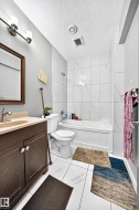 White tiled flooring, white subway-style shower wall tile, vanity with integrated sink, chrome faucet, and dark wood-finish cabinetry - 