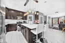 Kitchen with dark wood cabinetry, stainless steel appliances, a center island with a light-colored countertop, and a contemporary linear pendant light fixture - 12730 118 Street Nw, Edmonton, AB 