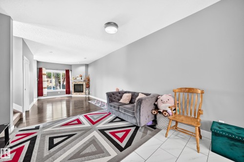 Spacious living area featuring wood-finish flooring, light grey wall tones, and a corner fireplace with stone surround - 12730 118 Street Nw, Edmonton, AB 