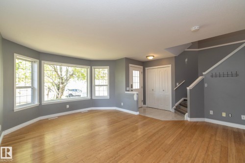 Hardwood-finish flooring, a bay window with multiple panes, a white front door with upper glass inserts, a double-door closet, and a staircase with white railings - 137 Michigan Street, Devon, AB 