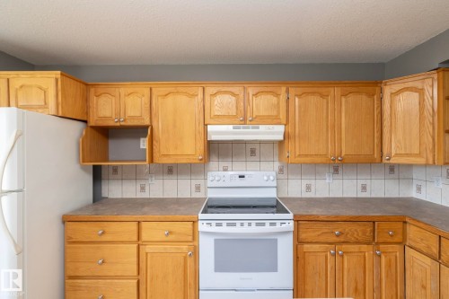 Kitchen featuring wooden cabinetry, laminate countertops, a white electric range, and a tile backsplash - 137 Michigan Street, Devon, AB 