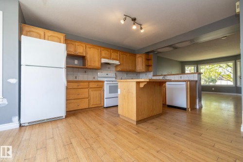 Kitchen with light wood-finish cabinetry, white appliances, and a central island with a breakfast bar - 137 Michigan Street, Devon, AB 