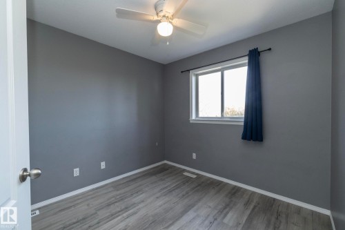 Light gray wood-finish flooring, neutral gray wall tones, ceiling fan with light fixture, and a window with white trim - 137 Michigan Street, Devon, AB 