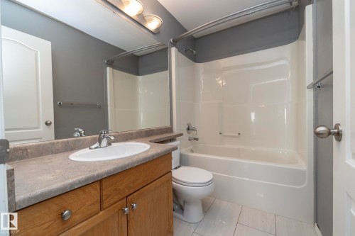 Bathroom featuring a wood-finish vanity with a built-in sink, a full-width mirror, a bathtub with an integrated shower, and light-toned floor tiles - 137 Michigan Street, Devon, AB 