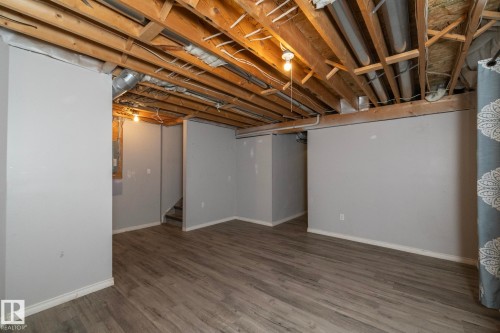 Finished basement area featuring wood-finish flooring, light grey painted walls, exposed ceiling joists, and a staircase - 137 Michigan Street, Devon, AB 