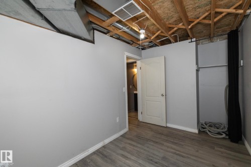 Wood-finish flooring, light gray painted walls, a white paneled door, and exposed ceiling joists - 137 Michigan Street, Devon, AB 