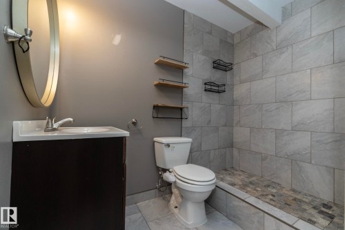 Contemporary bathroom featuring a dark wood-finish vanity with a white integrated sink, a large oval mirror, and a tiled shower stall with a pebble-finish floor - 137 Michigan Street, Devon, AB 