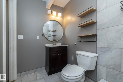 Vanity with a white countertop and round mirror, contemporary wall-mounted lighting, and light wood-finish shelving - 137 Michigan Street, Devon, AB 