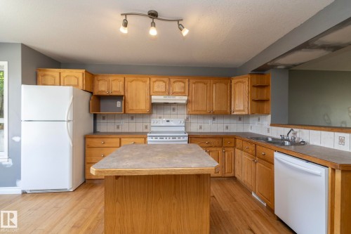 Kitchen featuring wood-finish cabinetry, a central island, a double basin sink, and a tile backsplash - 137 Michigan Street, Devon, AB 