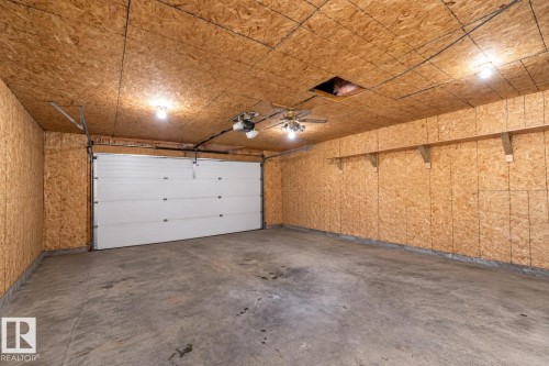 Expansive garage space with a large white sectional door, concrete flooring, and built-in shelving - 137 Michigan Street, Devon, AB 