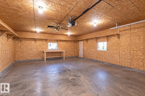 Spacious garage with concrete flooring, exposed oriented strand board walls and ceiling, surface-mounted lighting, and a ceiling fan - 137 Michigan Street, Devon, AB 
