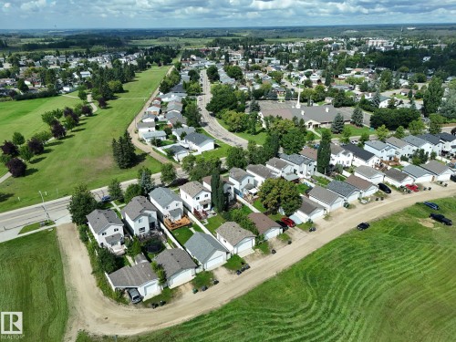 Aerial view of a residential neighborhood with detached homes, surrounded by expansive green spaces and mature trees - 137 Michigan Street, Devon, AB 
