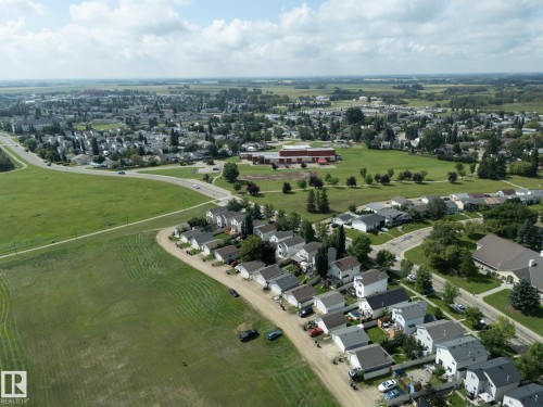 Expansive aerial perspective showcasing a residential neighborhood with surrounding green spaces and distant agricultural fields - 137 Michigan Street, Devon, AB 