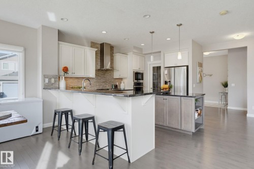 Kitchen featuring white cabinetry, dark countertops, a mosaic tile backsplash, stainless steel appliances, and a central island with storage - 9448 228 Street Nw, Edmonton, AB 