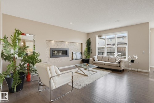Wood-finish flooring throughout, large window, built-in fireplace with stone-look surround, recessed lighting, and ceiling-mounted speaker - 9448 228 Street Nw, Edmonton, AB 