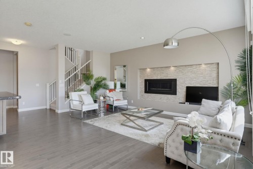 Open-concept living space featuring wood-finish flooring, a built-in electric fireplace with stone surround, recessed lighting, and a contemporary staircase with white risers and railings - 9448 228 Street Nw, Edmonton, AB 