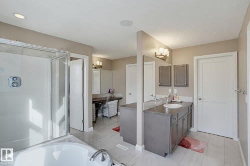 Walk-in shower with clear glass enclosure, soaking tub with chrome fixtures, double vanity with gray cabinetry and white round sink, built-in vanity desk, and recessed ceiling lighting - 9448 228 Street Nw, Edmonton, AB 