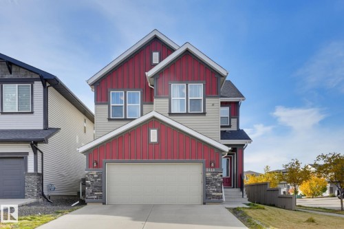 Two-story residence featuring vertical red and horizontal beige siding, an integrated garage with a light-colored door, stone accents on the garage and entryway, and prominent gabled rooflines - 9448 228 Street Nw, Edmonton, AB 