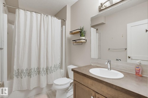 Bathroom with a white tub and shower combination, chrome shower rod, vanity with a rectangular sink, chrome faucet, and a large wall-mounted mirror - 9448 228 Street Nw, Edmonton, AB 