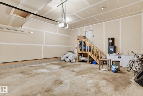 Spacious garage featuring concrete flooring, unpainted drywall walls, a wood staircase, an overhead garage door opener, and recessed ceiling lighting - 9448 228 Street Nw, Edmonton, AB 