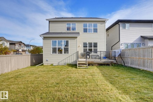 Expansive backyard with a wooden fence, large grassy area, and a raised deck featuring metal railings - 9448 228 Street Nw, Edmonton, AB 