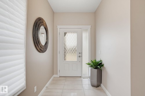 Entryway featuring a white door with diamond-patterned glass, coordinating sidelight, and light-toned tile flooring - 9448 228 Street Nw, Edmonton, AB 