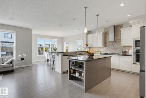 Modern kitchen featuring white cabinetry, stainless steel appliances, a stone-finish island with shelving, and light wood-finish flooring - 9448 228 Street Nw, Edmonton, AB 