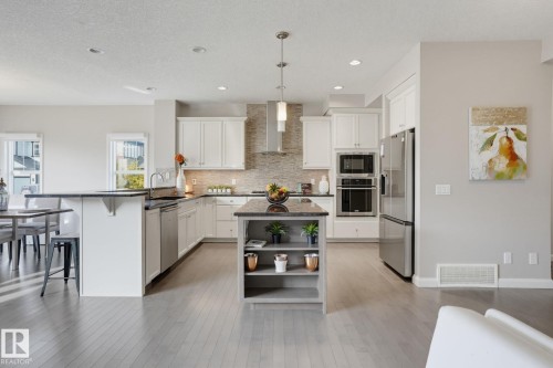 Gourmet kitchen featuring stainless steel appliances, a center island with open shelving, ample cabinetry, and dark stone countertops - 9448 228 Street Nw, Edmonton, AB 