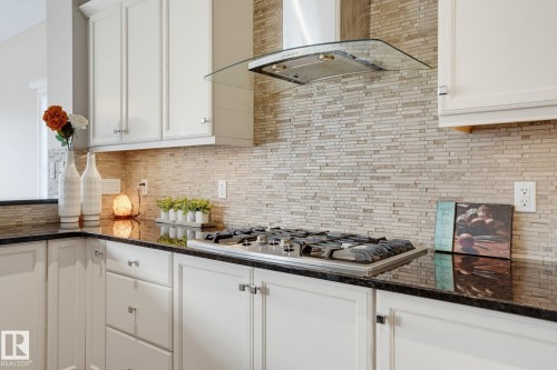 White cabinetry with brushed nickel hardware, dark countertops, a mosaic tile backsplash, and a stainless steel range hood - 9448 228 Street Nw, Edmonton, AB 