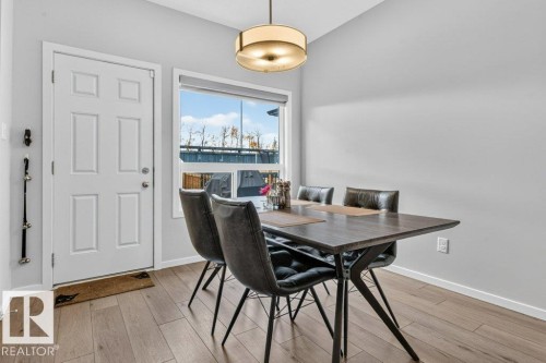 Recessed paneled entry door, wood-finish flooring, modern semi-flush mount light fixture, window with roller shade, and light-toned wall paint - 1020 Daniels Loop Sw, Edmonton, AB 