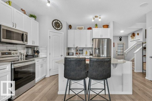 White cabinetry with stainless steel appliances, light wood-finish flooring, and a white subway tile backsplash - 1020 Daniels Loop Sw, Edmonton, AB 