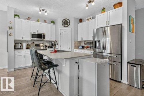 Kitchen featuring white shaker cabinetry, stainless steel appliances, light-toned wood-finish flooring, a kitchen island with seating, and track lighting - 1020 Daniels Loop Sw, Edmonton, AB 