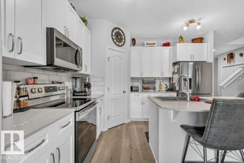 White shaker-style cabinetry with chrome hardware, stainless steel appliances, light-toned countertops, subway tile backsplash, and wood-finish flooring - 1020 Daniels Loop Sw, Edmonton, AB 