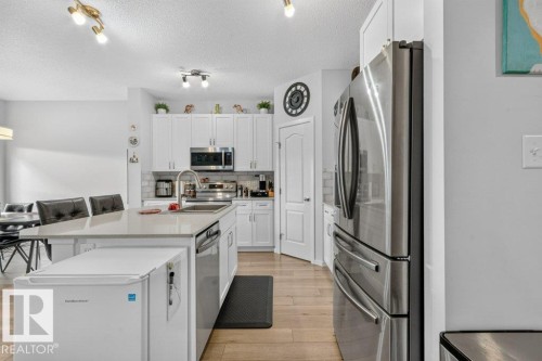 Kitchen featuring white cabinetry, stainless steel appliances, a center island with sink, light-toned countertops, and wood-finish flooring - 1020 Daniels Loop Sw, Edmonton, AB 