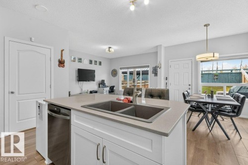 Kitchen island with double basin sink, stainless steel dishwasher, wood-finish flooring, and pendant lighting - 1020 Daniels Loop Sw, Edmonton, AB 