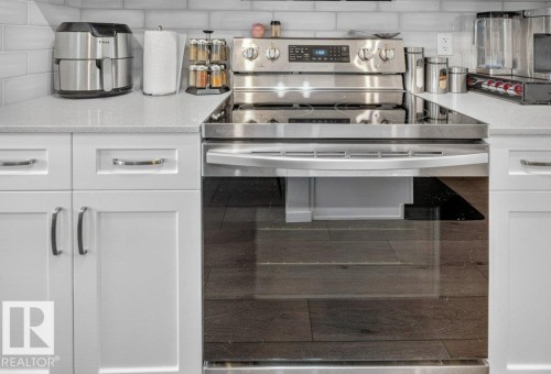 Stainless steel range with a smooth cooktop, white shaker-style cabinetry, light-colored countertops, and a subway tile backsplash - 1020 Daniels Loop Sw, Edmonton, AB 