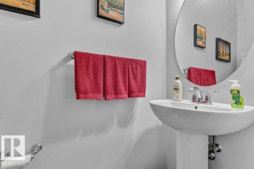 Pedestal sink with chrome faucet, circular wall-mounted mirror, and wall-mounted towel bar - 1020 Daniels Loop Sw, Edmonton, AB 