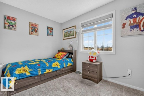 Light gray wall color, carpeted flooring, large window with blinds, wood-finish bed frame with built-in storage, and a matching wood-finish nightstand - 1020 Daniels Loop Sw, Edmonton, AB 